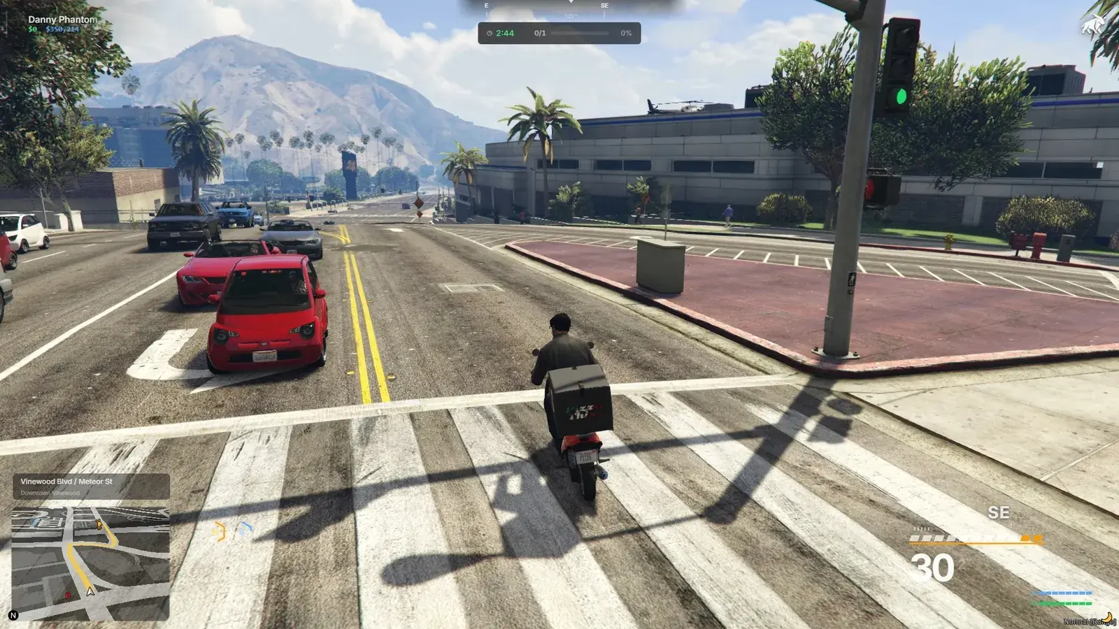 Delivery rider on a scooter carrying a Pizza This box across a Vinewood Boulevard intersection, with the delivery HUD timer and batch progress at the top and the minimap route below