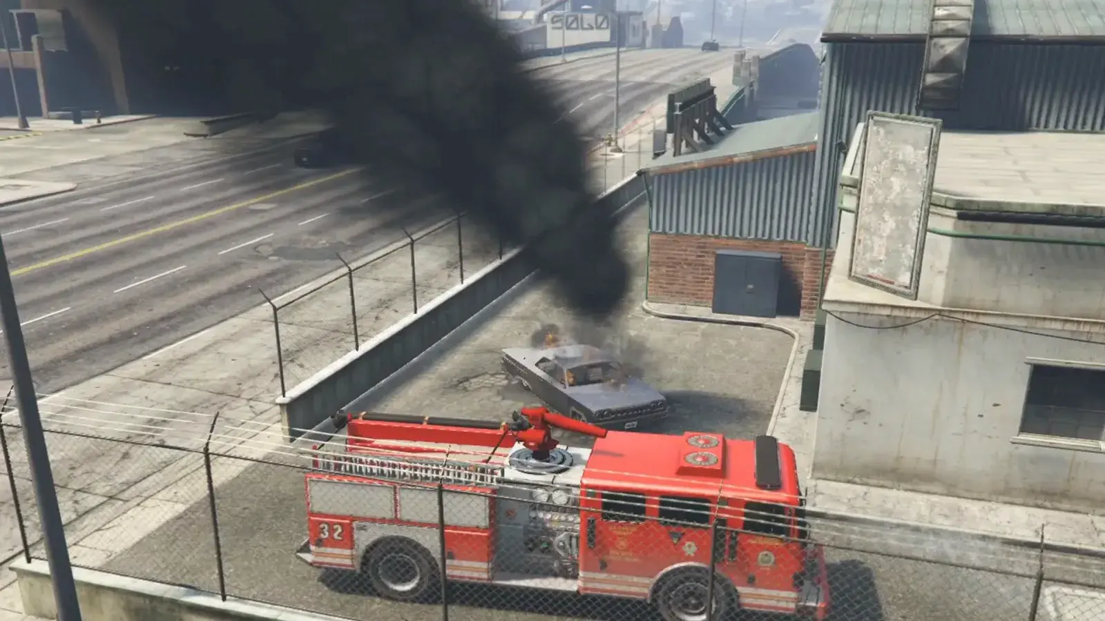 Engine 32 behind a chain-link fence, its roof cannon trained on a burning car under a column of black smoke
